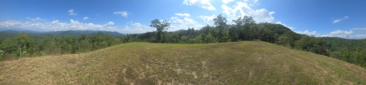 Grassy clearing with surrounding trees and distant ridges from the first Lot 6 stop